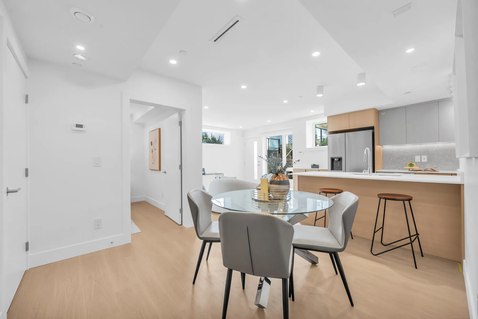 The dining room: a round glass table with grey chairs, the kitchen peninsula with two stools beyond