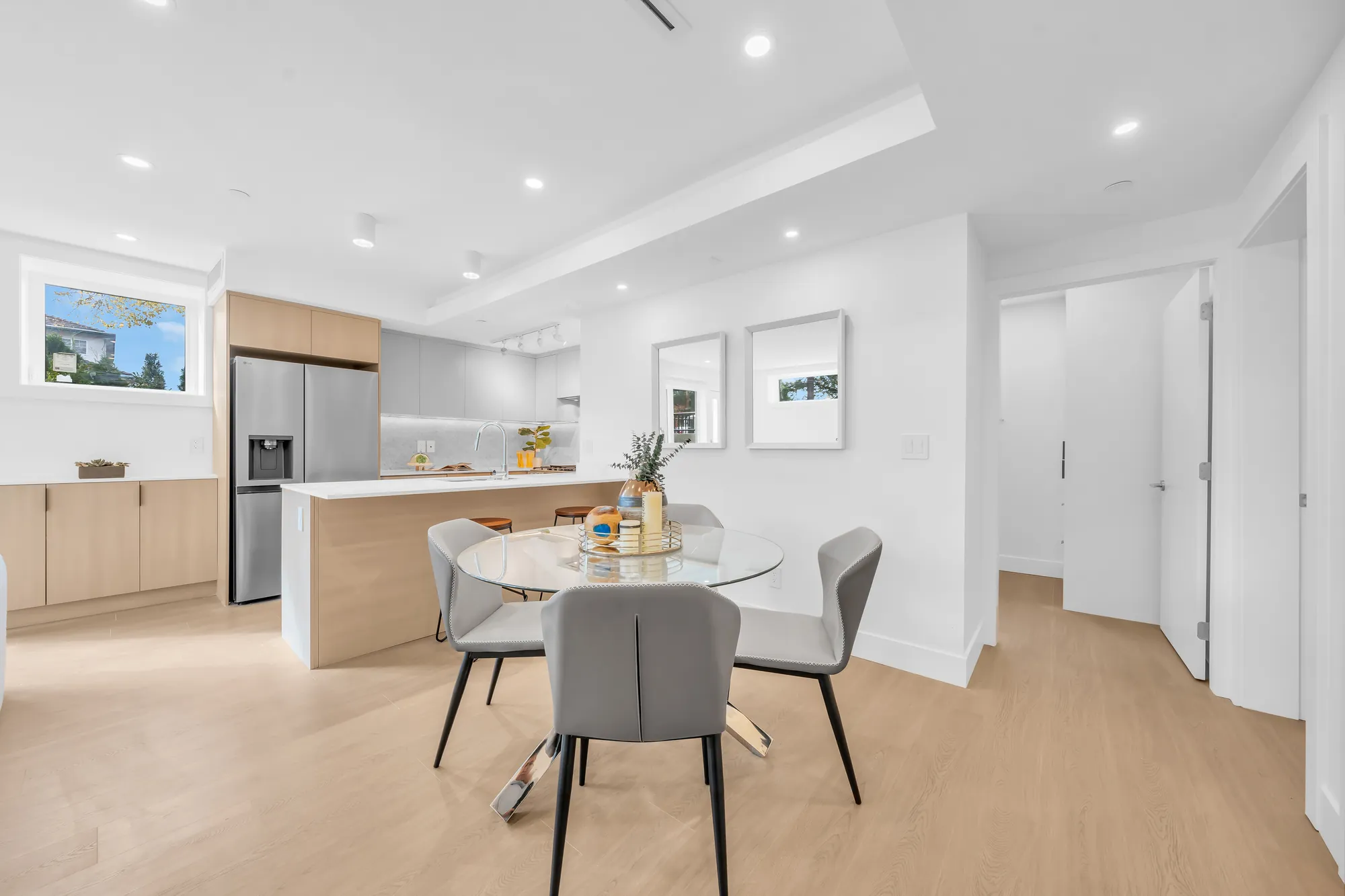 The dining table toward the kitchen: the stainless fridge, the peninsula, the hall to the bedrooms