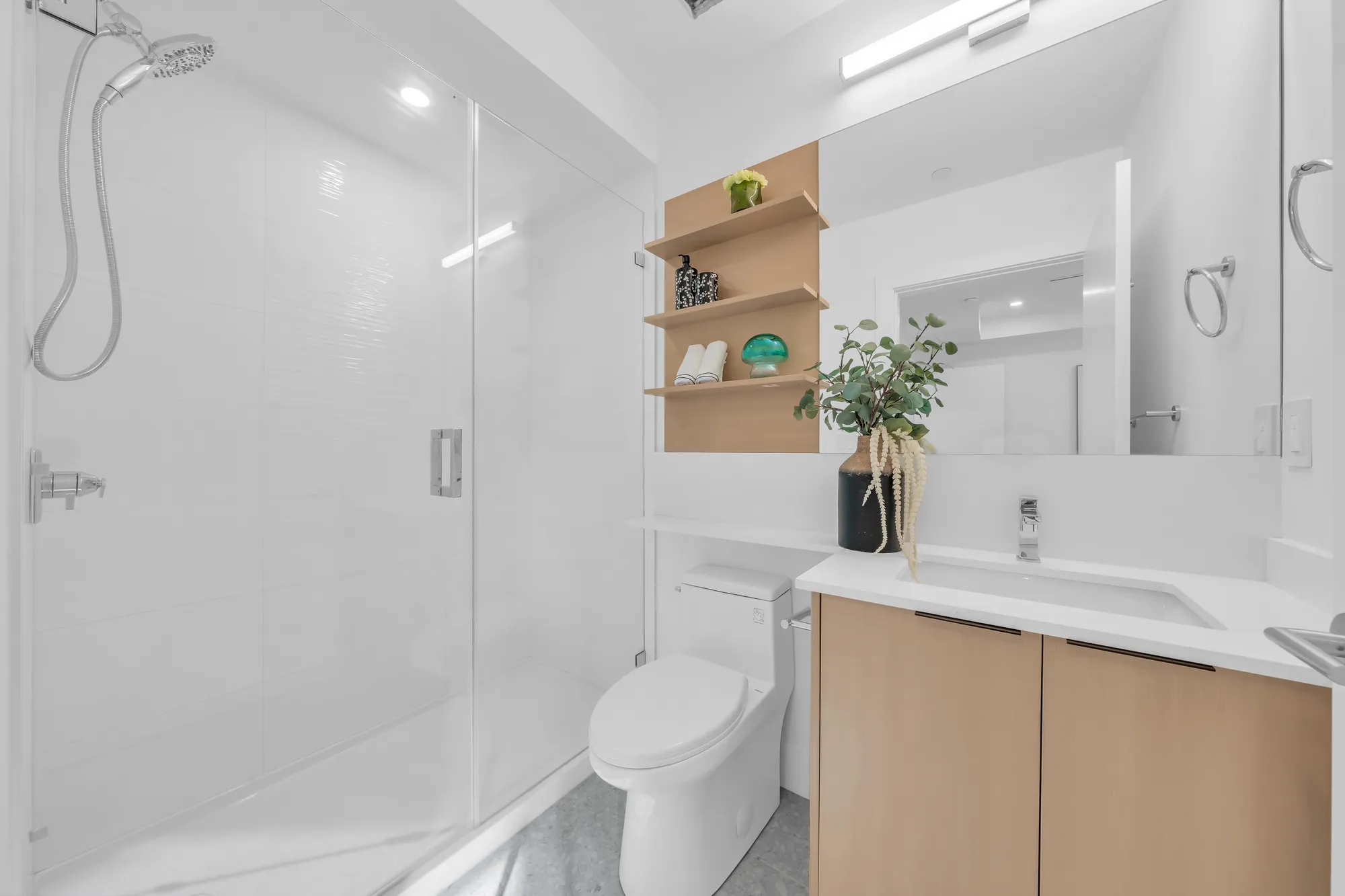 The primary bathroom: a glass shower, a toilet, an oak vanity with open shelves