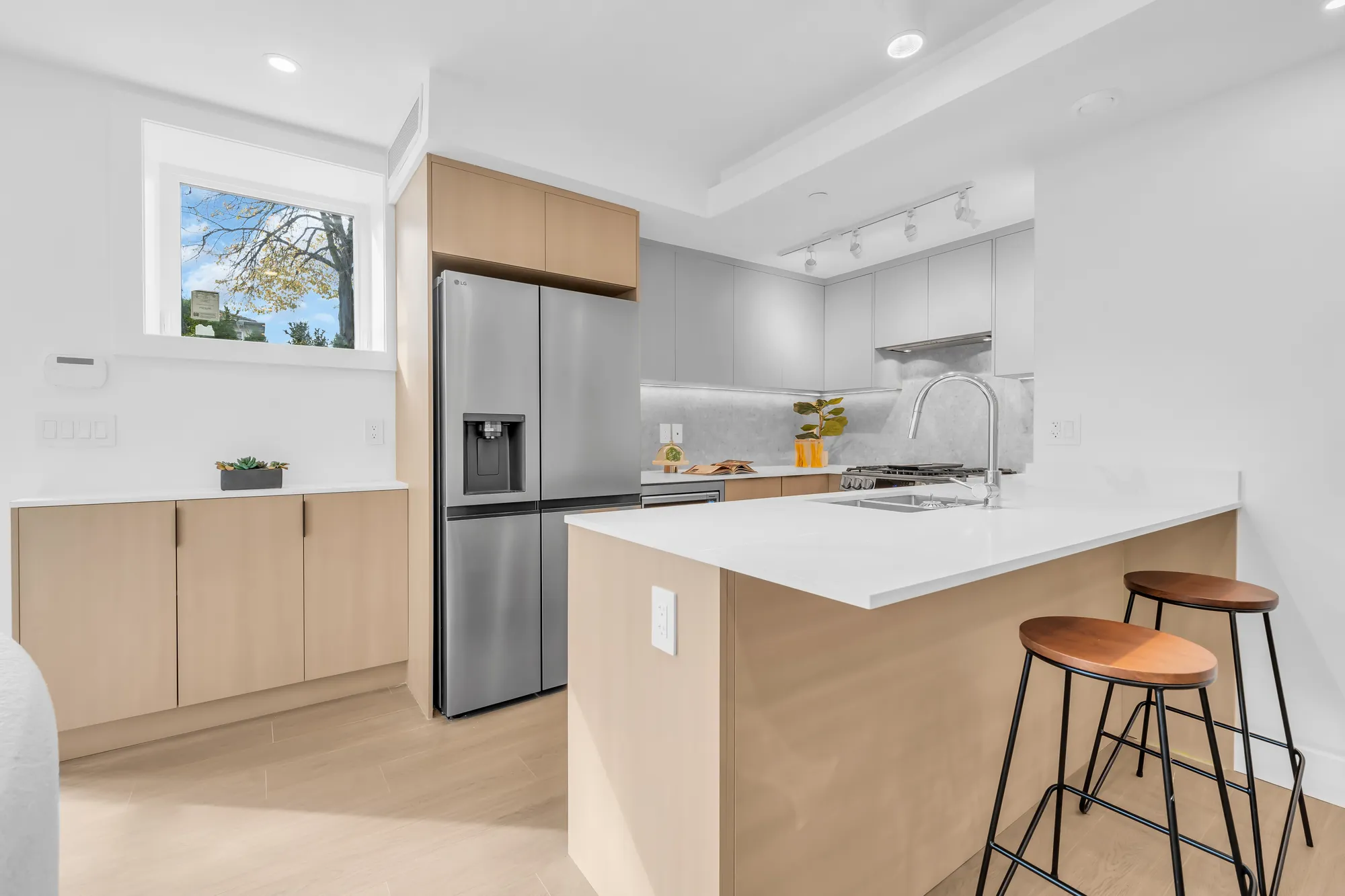 The kitchen: an L of oak and white cabinets with a peninsula and two wood stools, a stainless double-door fridge, a window