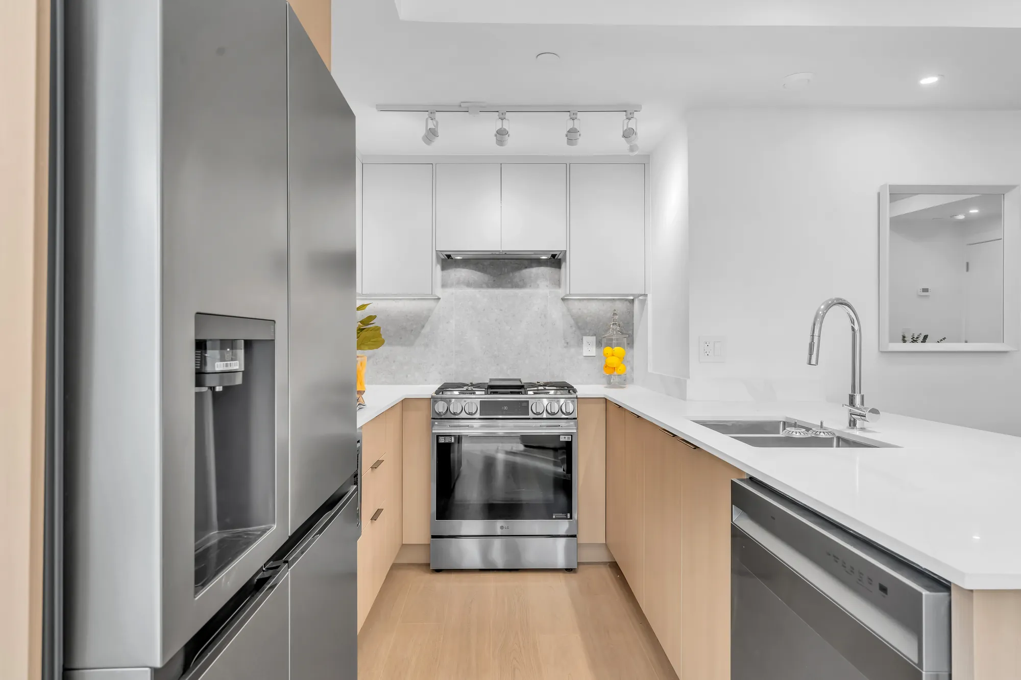 The fridge, the range and the sink, white upper cabinets and track lights