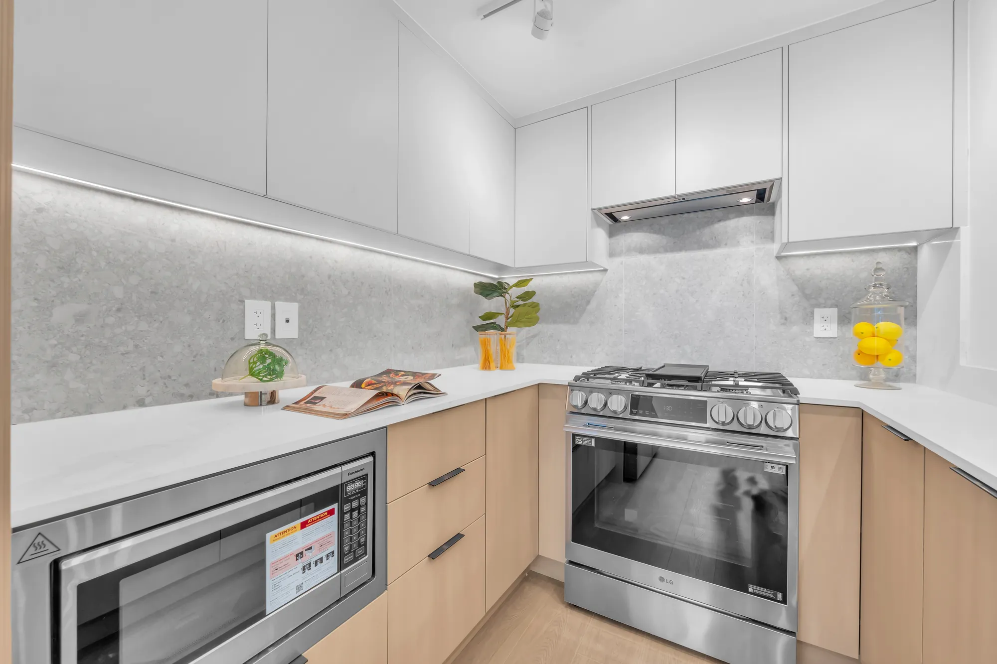 A stainless range under a hood, a built-in microwave, a grey stone backsplash