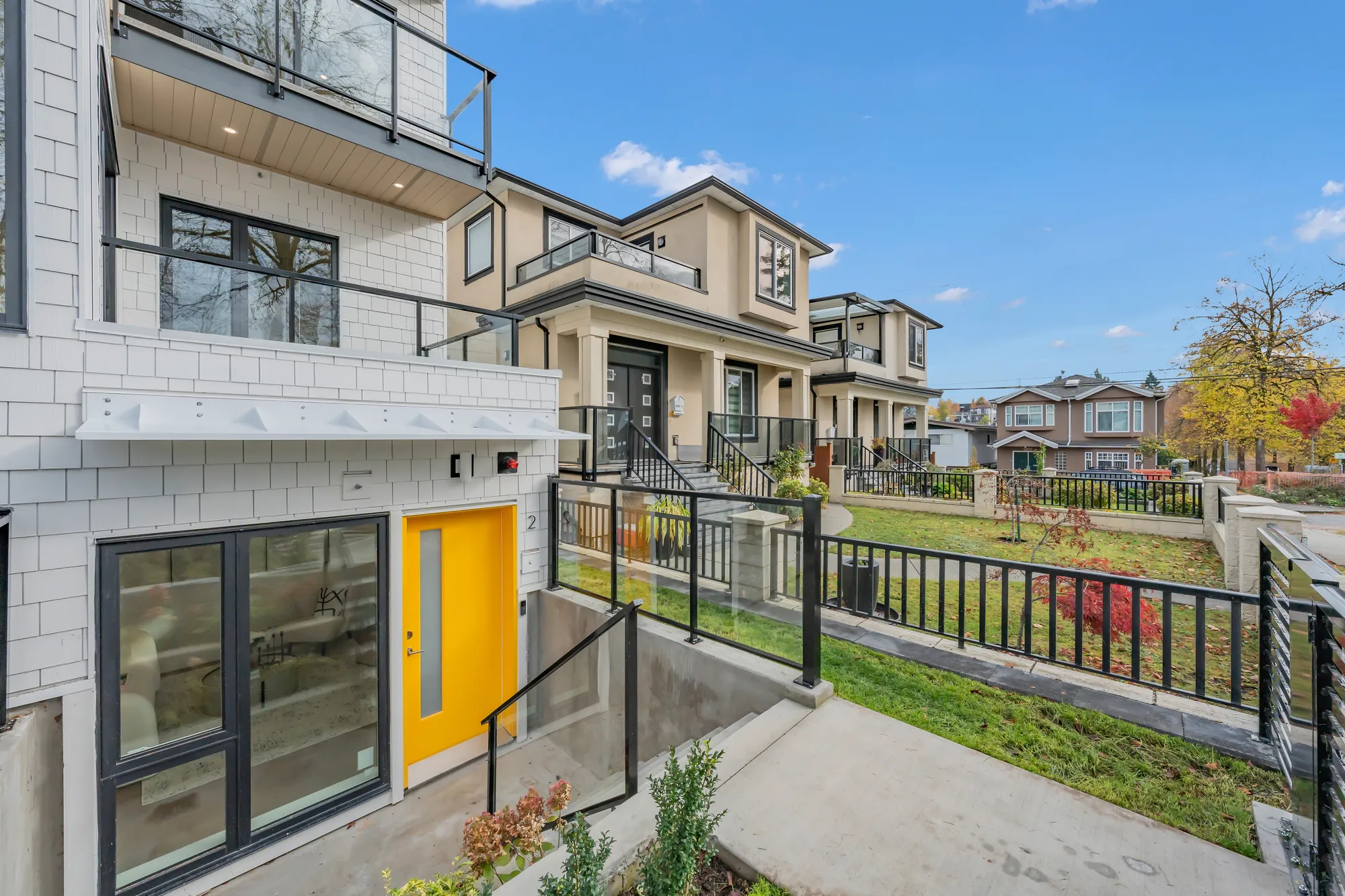 The sunken patio from above: the yellow door, a wide window, the glass railing and the lawn of the front yard