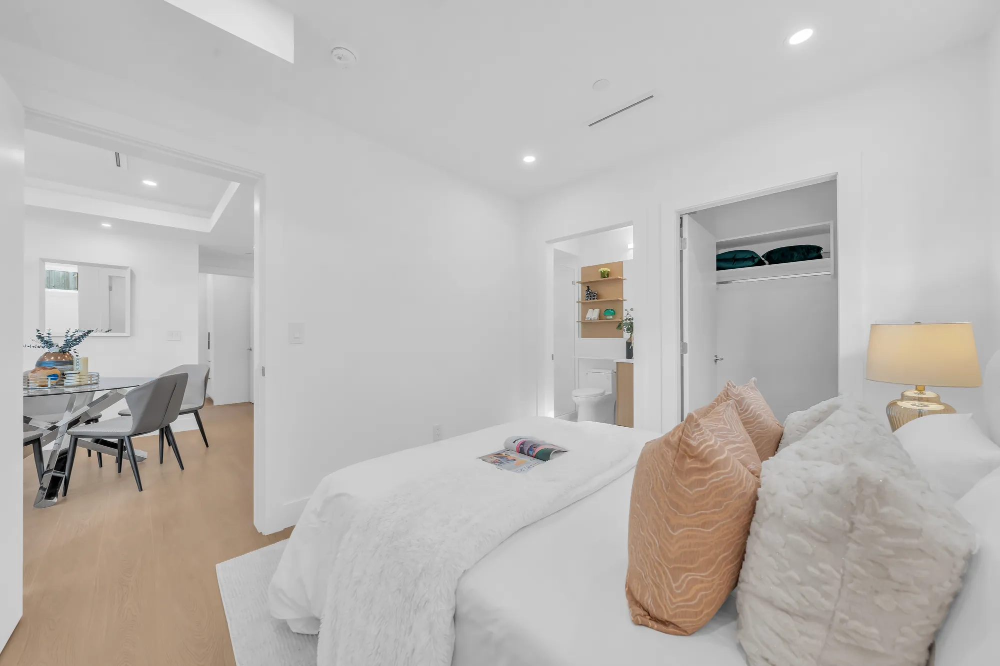 The primary bedroom toward the door: the bed, a lamp, the dining room beyond